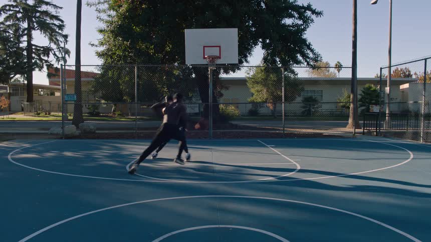 Two young black men playing basketball at an outdoor court in a suburban city during daytime