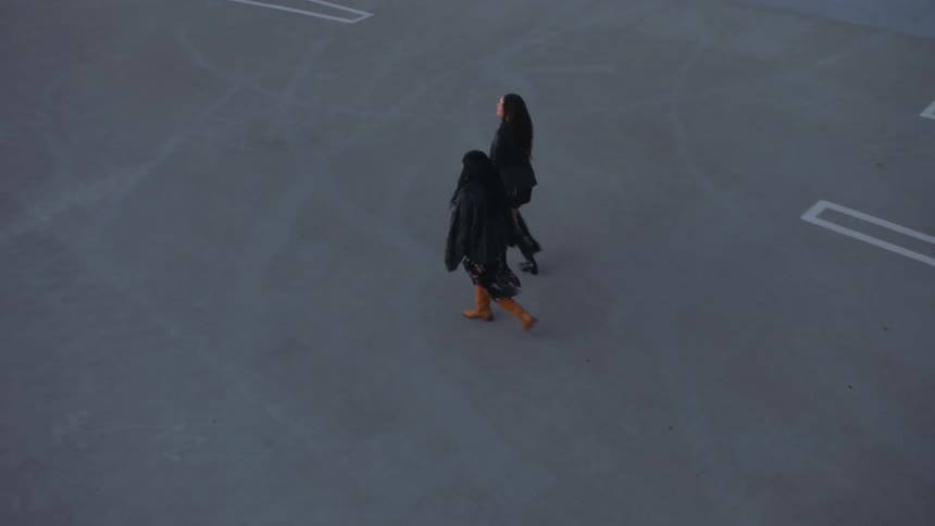 Two people walking across a large parking lot with marked parking spaces on the ground