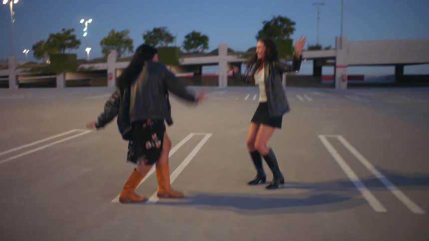 Two young female friends dancing together outdoors in an urban city at sunset