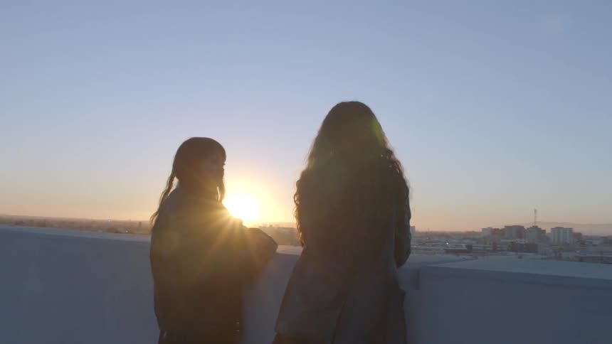 Two young women are standing with their backs turned looking at the sun on the horizon