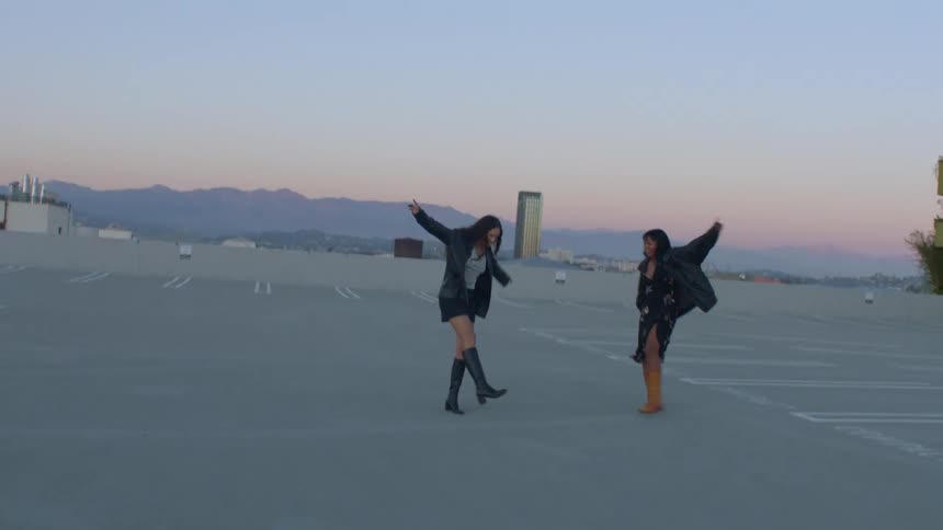 Two friends dancing joyfully together on a rooftop at sunset