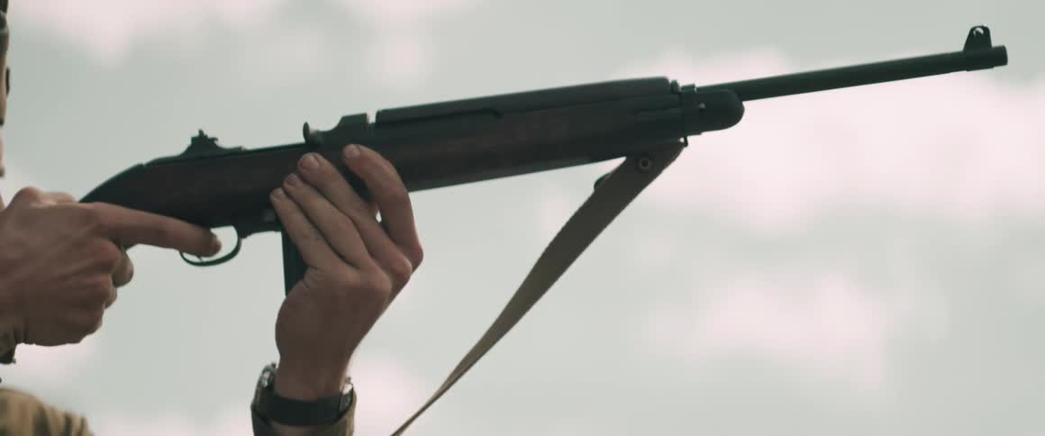 A soldier aims a rifle while standing outdoors in a focused stance