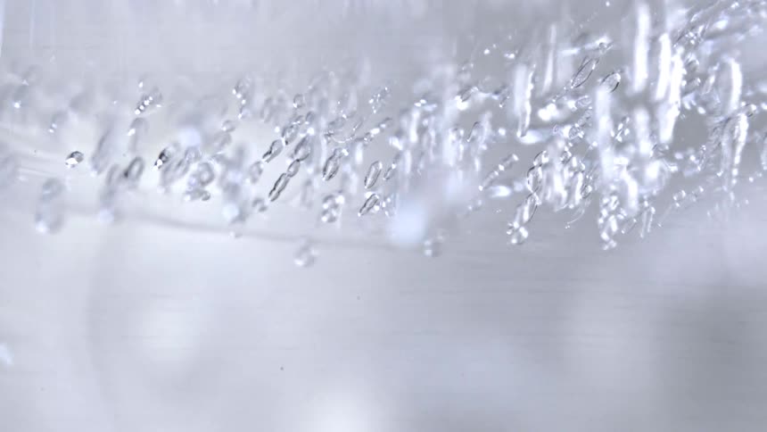 This macro footage captures a series of small elongated air bubbles trapped inside a dense layer of clear ice the frozen inclusions create a shimmering textured pattern that remains suspended within the translucent white and gray environment