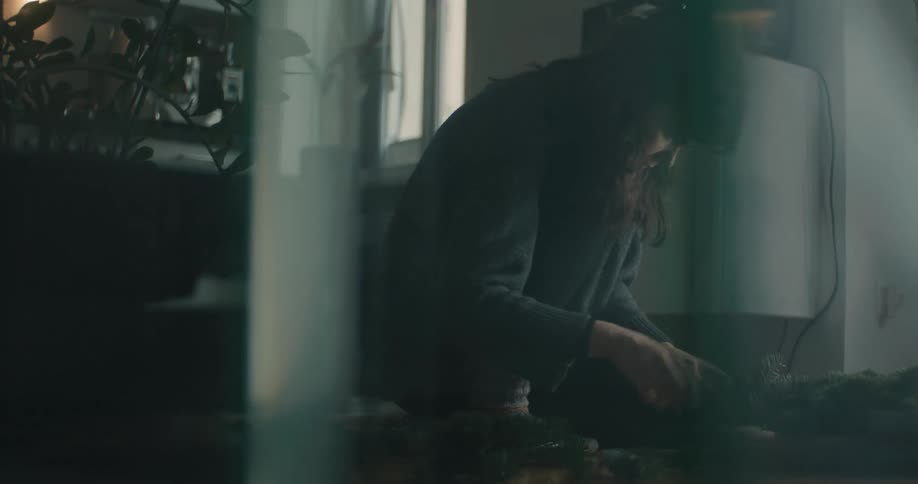 Woman seated indoors working with plants on a table near a window