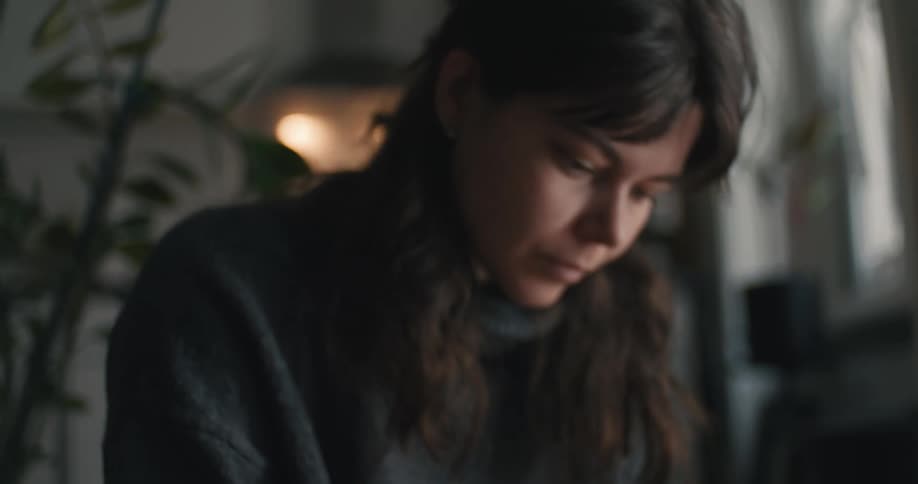 A close view shows a woman wearing a dark gray sweater as they carefully place white cylindrical candles into a lush green pine wreath indoors