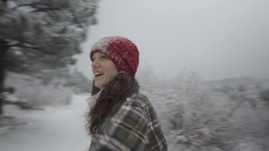 A young woman throws a snowball at another adult while standing in a wintry forest
