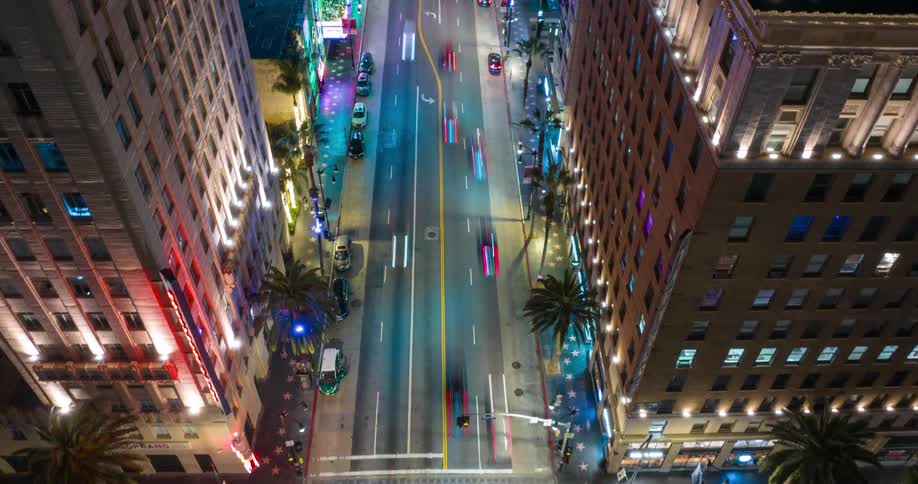 From high above a glowing intersection of Hollywood Boulevard and Vine Street the view flies down the boulevard at night as streaking car lights flow between towering illuminated buildings