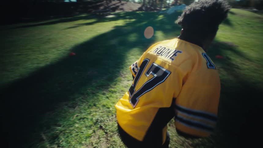 A young black male athlete practising american football on a lawn outdoors during daytime