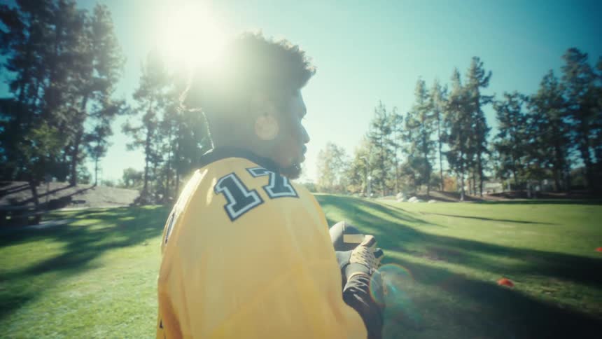 The man is holding a football on the green grass