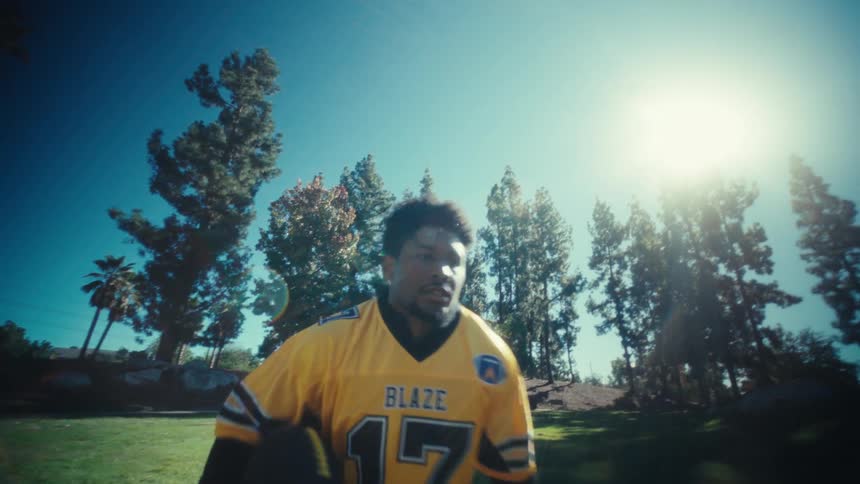 Man runs on a field in the park carrying a football on a sunny autumn day