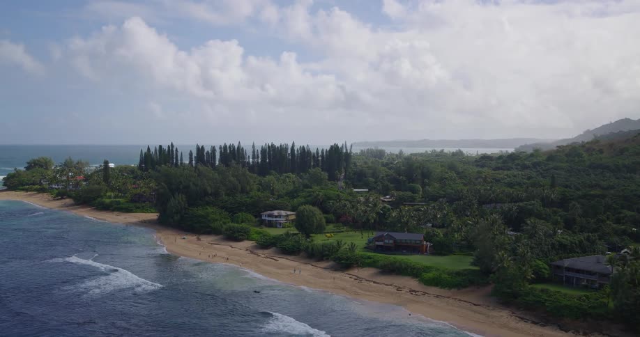 Aerial view of gentle waves rolling onto a sandy tropical coastline bordered by lush greenery
