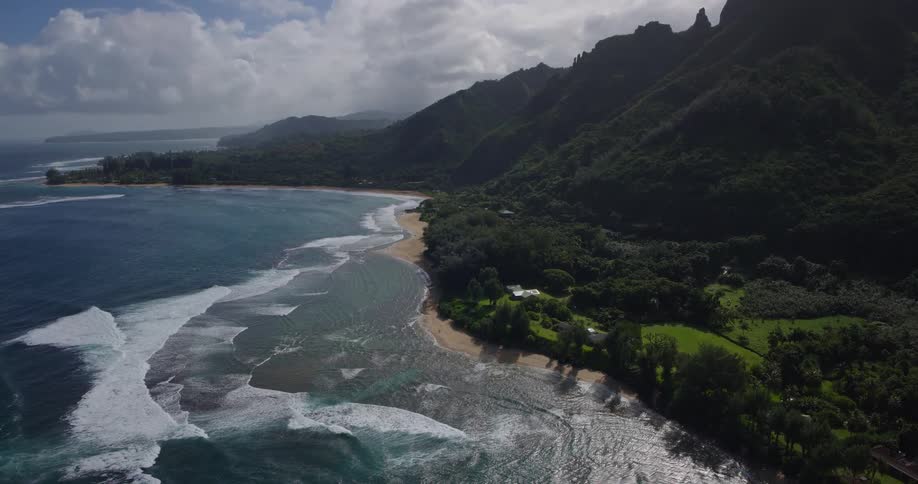 Aerial view of tropical coastline with jagged mountains and waves hitting the sandy beach