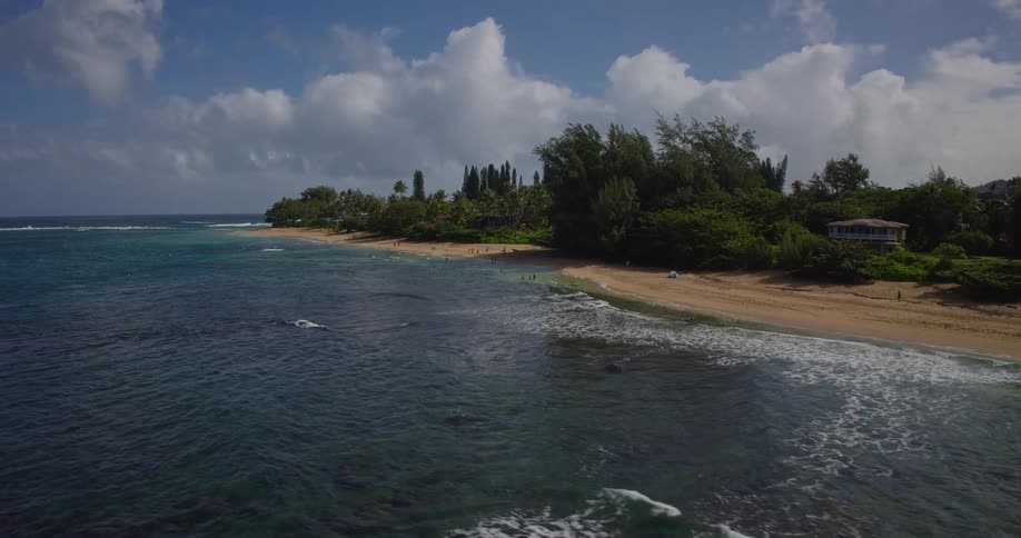 House among tropical trees stands out near beach with clear waves and partly cloudy sky