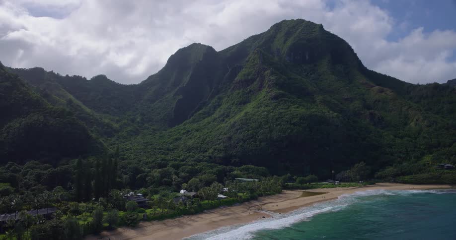 Aerial view of a tropical coastline with verdant mountains and waves breaking on a sandy beach