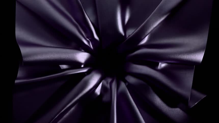 A shimmering dark purple fabric is drawn into a central point twisting into elegant folds and shifting highlights before being sucked into a deep black void as the material vanishes completely