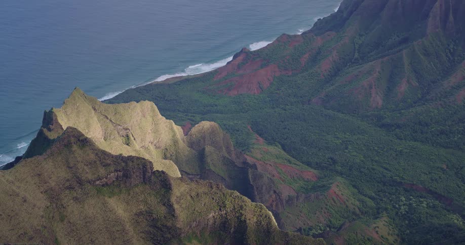 Coastal mountain range with steep peaks and dense vegetation receives sunlight over shaded valleys