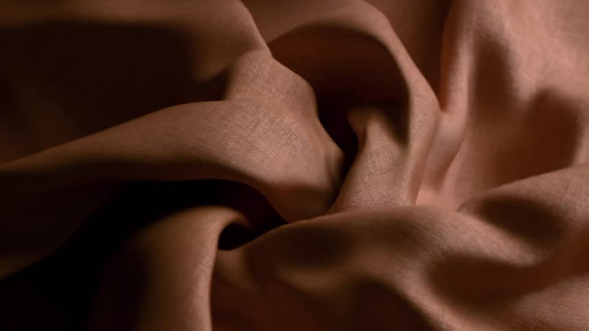 A close view shows smooth brown fabric swirling and folding in a spiral motion as soft light creates deep shadows within the layers