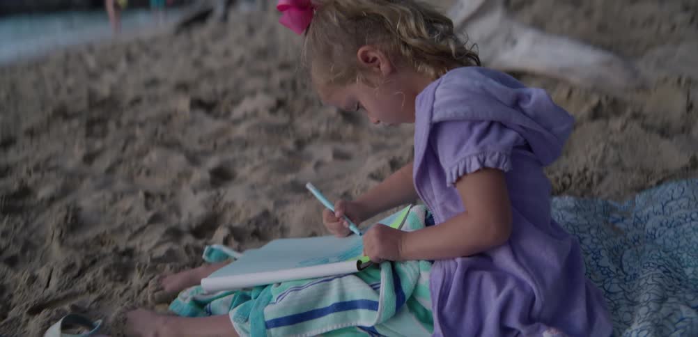 Child sitting on the sand drawing in a notebook outdoors