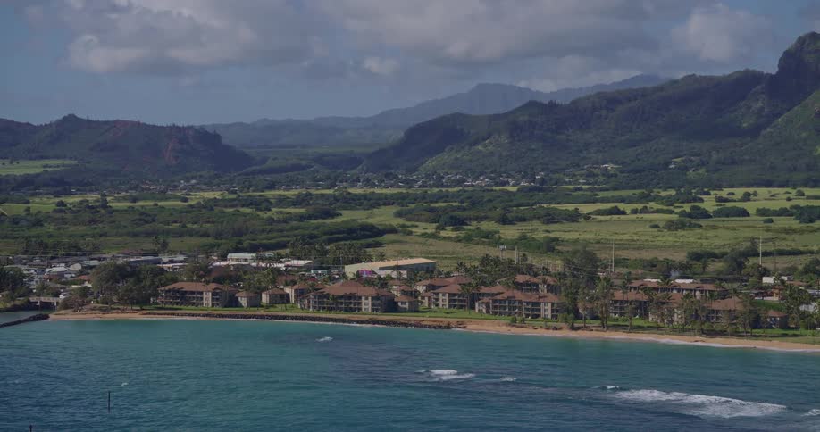 Aerial view shows a coastal strip with blue ocean beachfront buildings and mountains in the background
