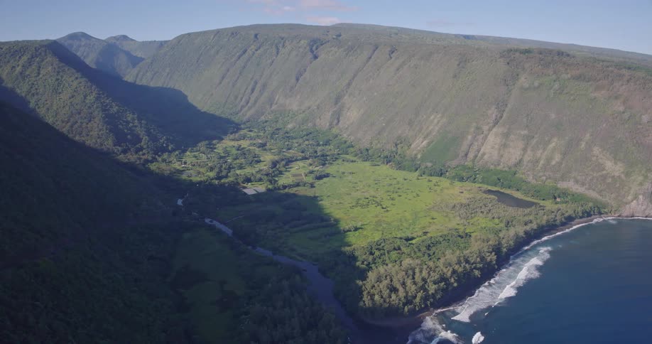 Green valley with winding river is surrounded by steep cliffs and beach with breaking waves