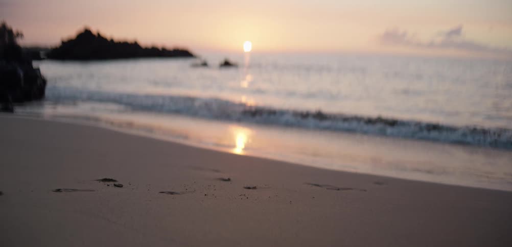 A beach at sunset ocean waves rolling onto the shoreline as the orange sun sinks in the distance