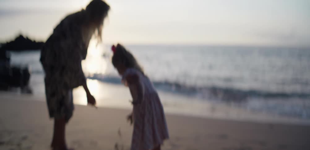 Mother and daughter build a sand castle on a quiet beach at sunset