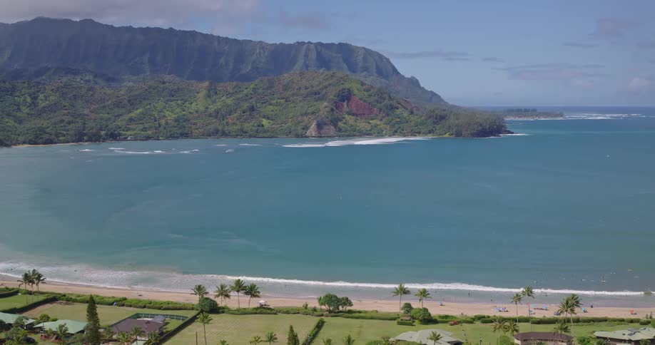 Resort along the coastline at midday with bright sunlight reflecting off the water and a mountain rising in the background
