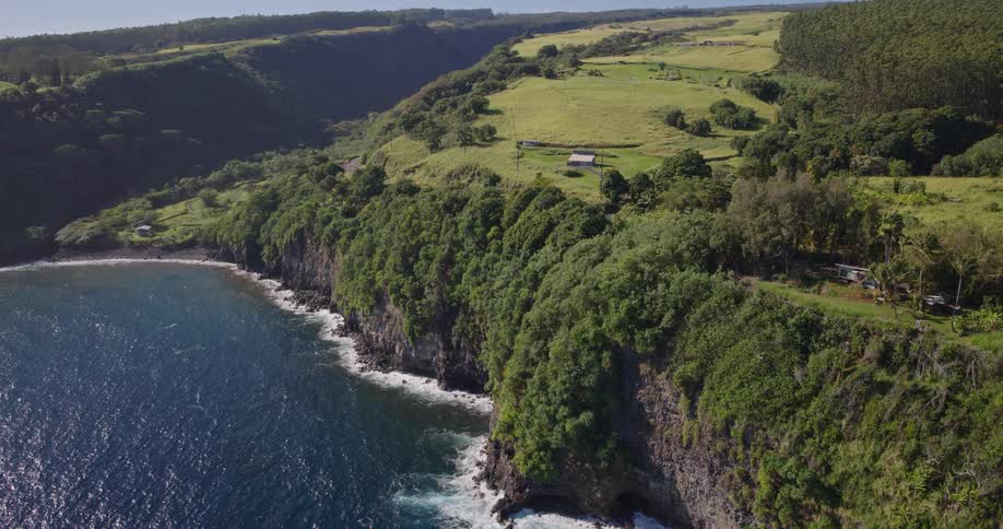 Cliffs covered in vegetation descend to curved beach with blue waves and open fields above