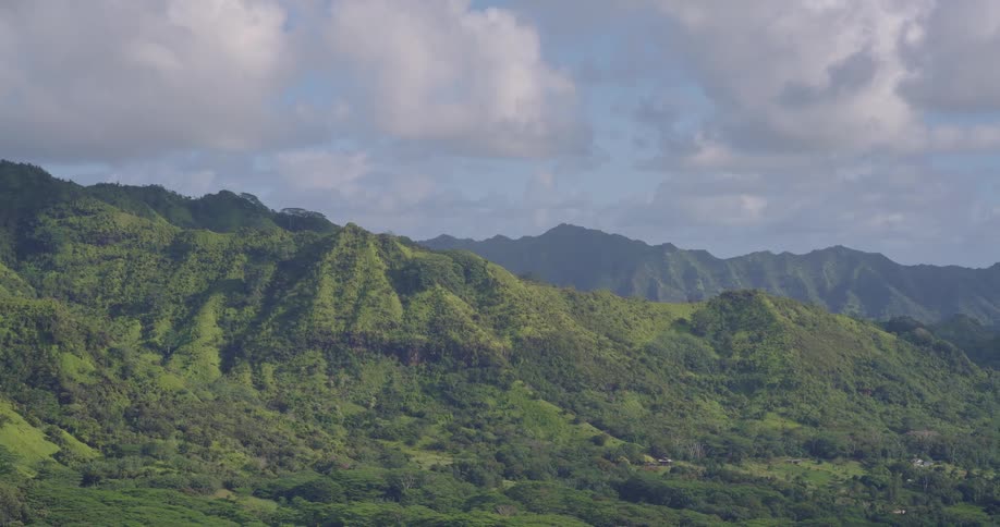 Aerial view shows mountains covered with green vegetation under a partly cloudy sky