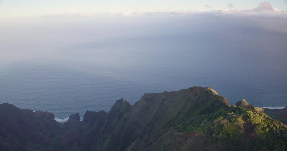 A sweeping aerial view of jagged mountain peaks rising from the ocean with misty clouds rolling over the horizon