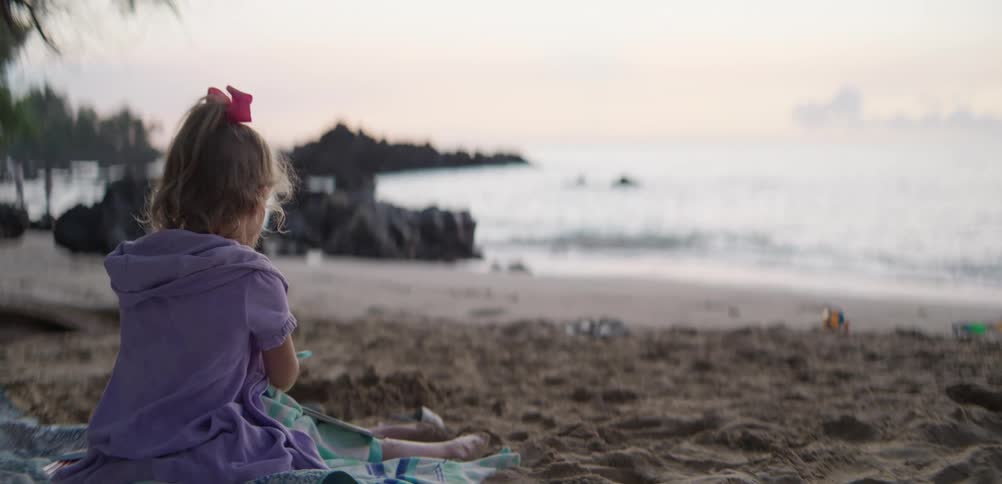 Girl colors while sitting on a blanket on the beach