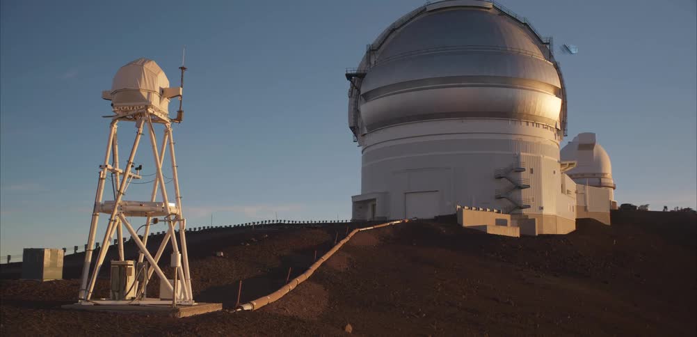 Astronomical observatory with metallic domes rises over barren terrain lit by evening sunlight