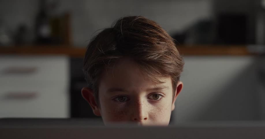 A young boy intensely focuses on a screen in a softly lit room