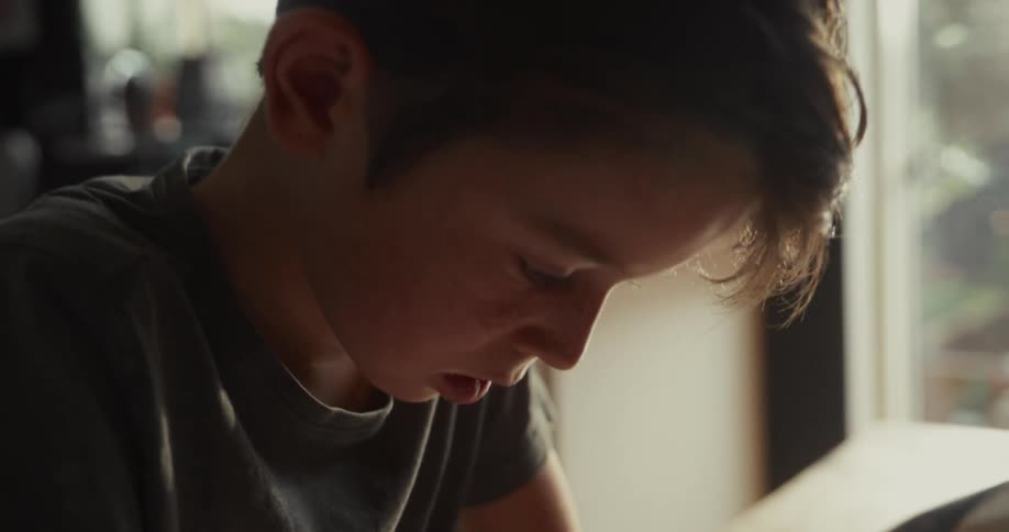 A young boy studies and writes at a wooden table inside a quiet room