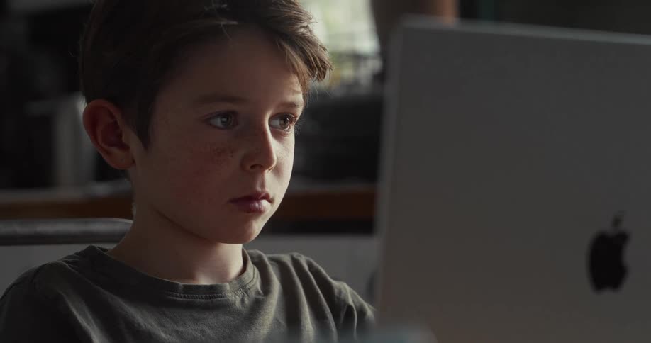 Boy sitting at a table looking at a laptop computer screen