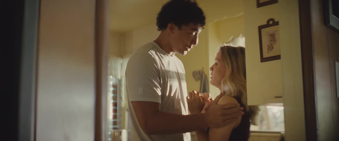 A man holds a womans shoulders in a hallway while she speaks to him with an emotional and distressed expression she eventually pulls away and walks past him into the kitchen ending their brief and tense interaction