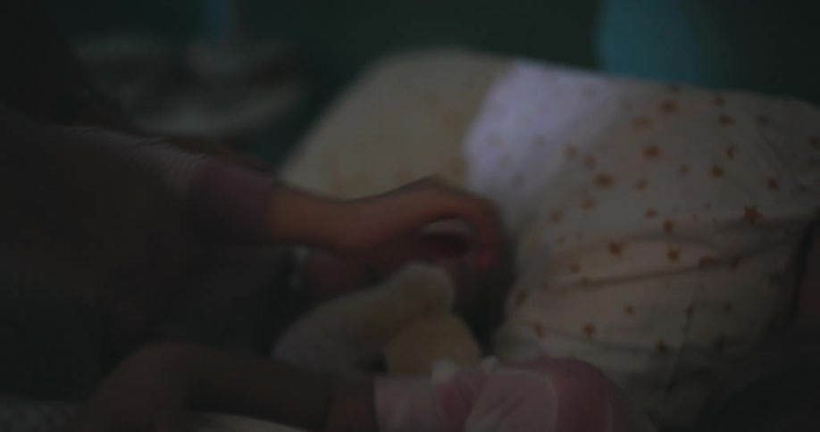 A woman is in a dimly lit bedroom tucking in two children in a bed