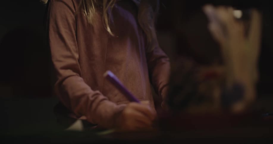 A child wearing glasses sitting indoors writing on a piece of paper with focus and concentration