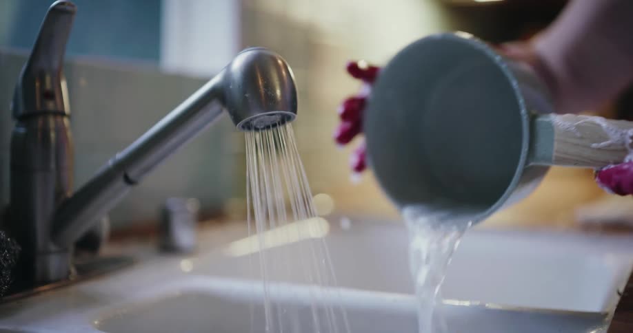 A persons gloved hands are washing a pot at a sink in a kitchen