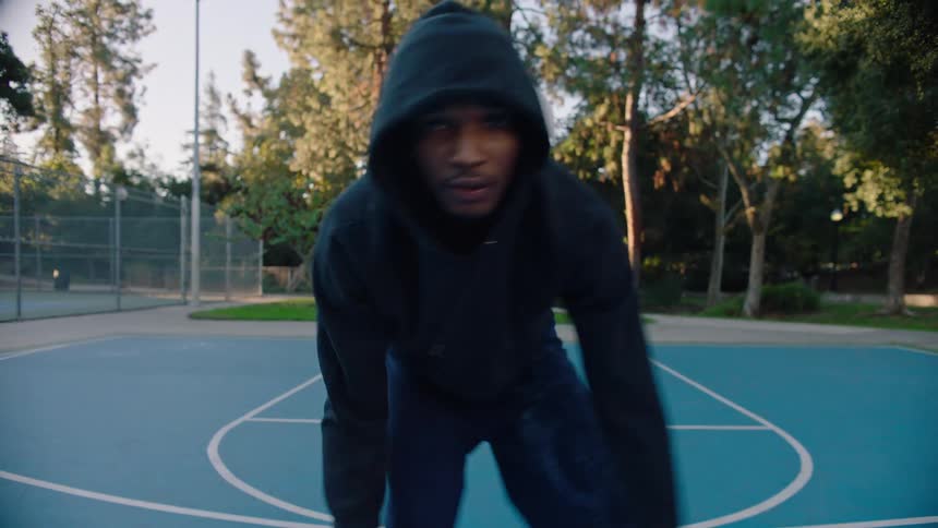 Person dribbles a basketball on an outdoor court surrounded by trees