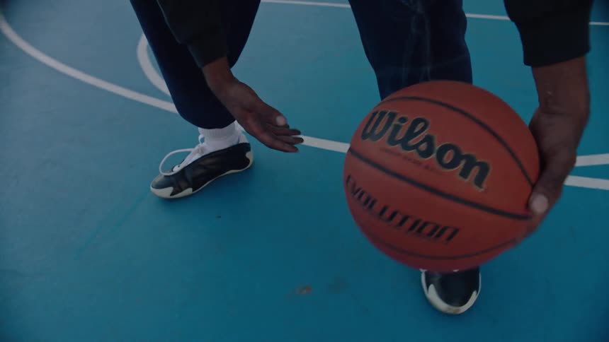 Black male hands dribbling a basketball between the legs outdoors at a basketball court