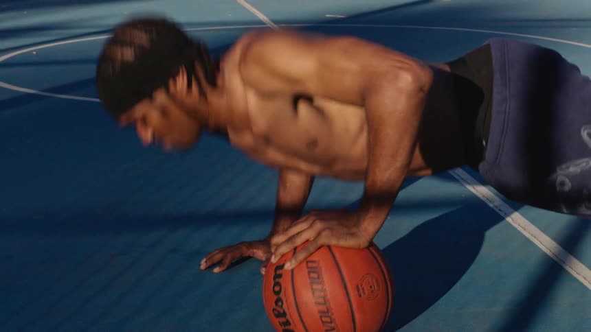 Close up of a young black male athlete performing push ups with a basketball at an outdoor court during daytime