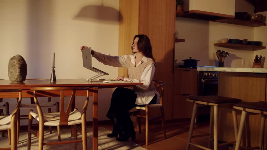 Woman sits at a table and opens the lid of her laptop computer