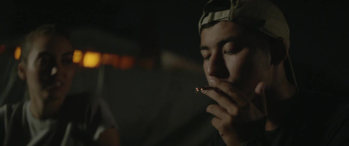 A man lights a cigarette with a woman sitting nearby