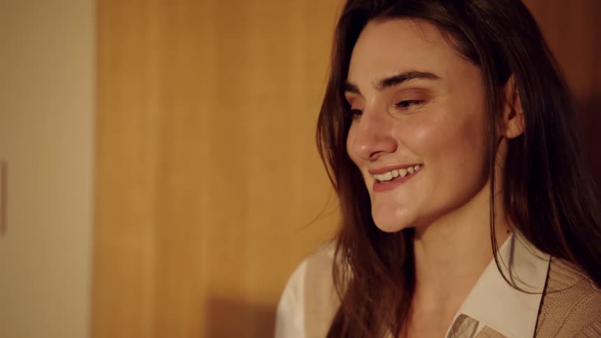 A young woman sitting behind a computer on a conference call smiling warmly as she speaks