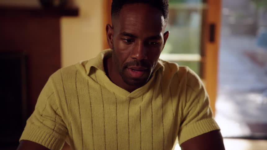 Man sitting indoors talks while viewing a laptop during the daytime