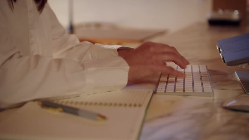 Woman typing on a computer keyboard stops to write in a notebook