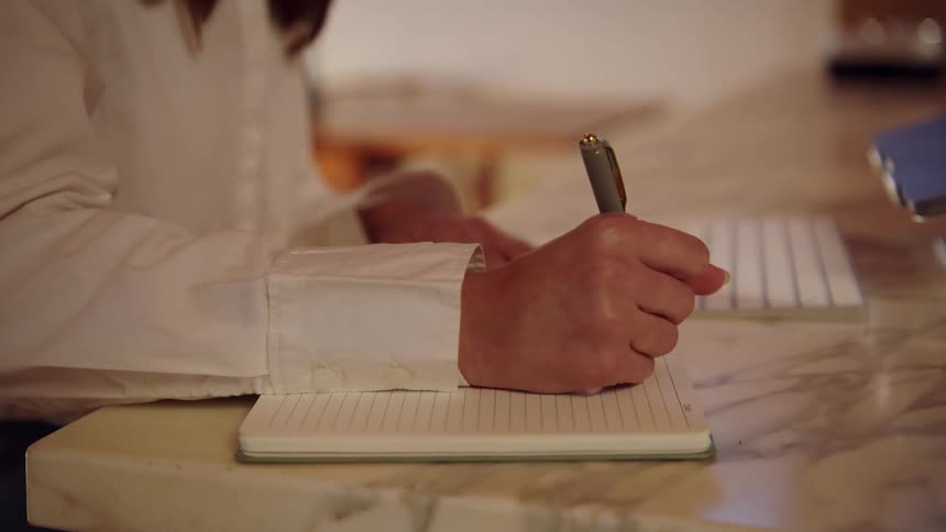 Woman typing on a computer keyboard stops to write in a notebook