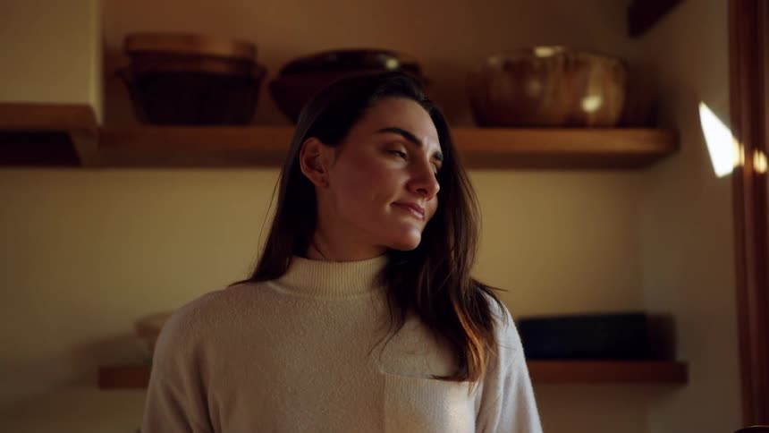 Woman holding a mug smiles and looks out the kitchen window