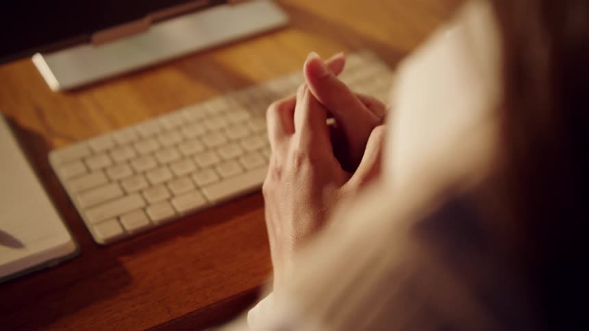 Close up of a young woman rubbing her hands anxiously while sitting at a digital worktable in an office during daytime